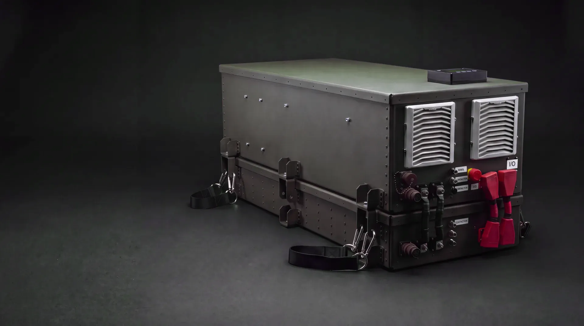 The SPM Power Export Kit (PEK) on a dark studio backdrop: an olive-drab enclosure with cooling vents, a status display, an emergency stop and power connectors on its end panel